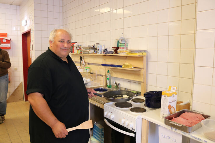 Ein Mann steht vor einem Elektroherd mit Kochlöffel in der Hand und blickt lächelnd in die Kamera (Bild: FSW)