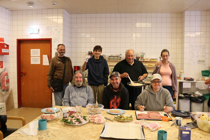 Die Kochgruppe von Forum Obdach Wien posiert gemeinsam an einem mit diversen Speisen gedeckten Tisch für das Foto (Bild: FSW)