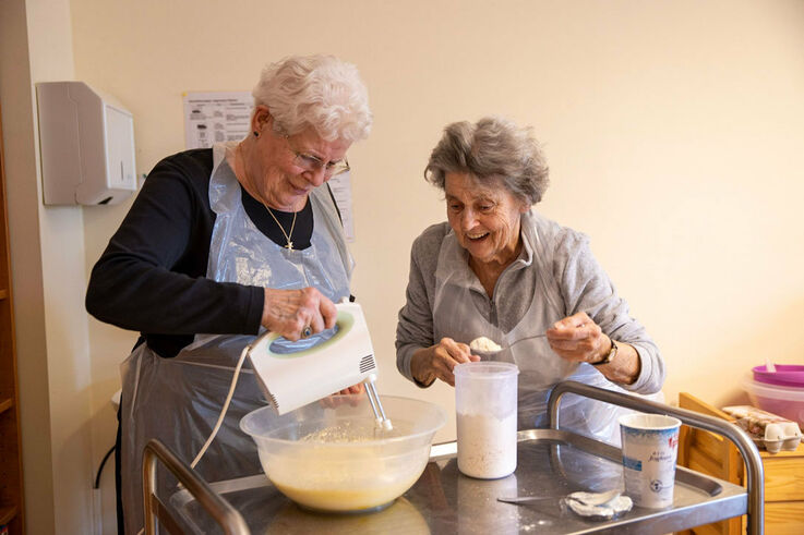 Zwei Teilnehmerinnen eines Kochworkshops im Tageszentrum mixen gerade eine Art Teigmasse mit einem Handmixer und lachen dabei (Bild: FSW)