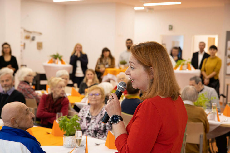 FSW-Geschäftsführerin Anita Bauer spricht mit Mikrofon in der Hand an ein Publikum beim Showcooking zur Neueröffnung des Tageszentrums Heigerleinstraße (Bild: FSW)